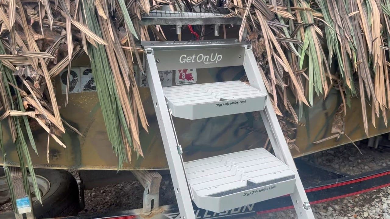 The nautiDAWGS ladder mounted on a camo-wrapped Allison hunting boat dressed in blind grass